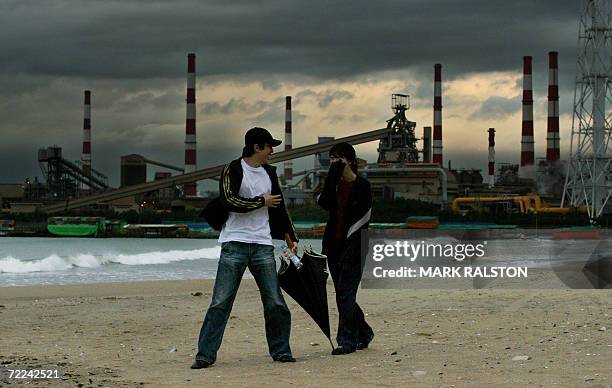 Pohang, REPUBLIC OF KOREA: A South Korean couple enjoy a beach walk during a thunderstorm with the POSCO companies flagship steel mill and...