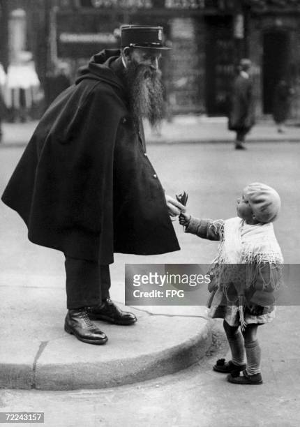 Little girl hands a posy of lily-of-the-valley to officer Leclerc, who is on duty at the Porte Saint-Denis in Paris, circa 1920. It is the custom to...
