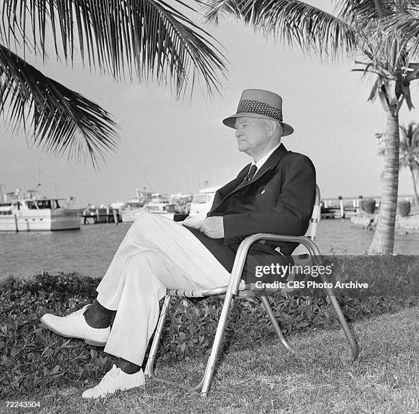 Former American president Herbert Hoover weras a hat as he sits on a lawn chair and looks over the water outside his cottage for an episode of the...