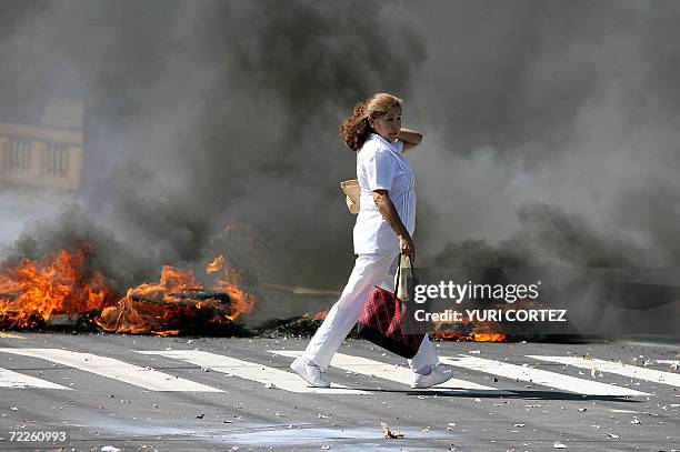 San Salvador, EL SALVADOR: Una enfermera pasa frente a neumaticos en llamas que bloquean una de las principales calles de acceso al Hospital Rosales...