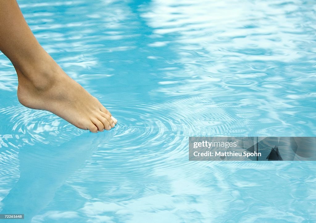 Woman touching surface of water with toe, close-up of foot and water