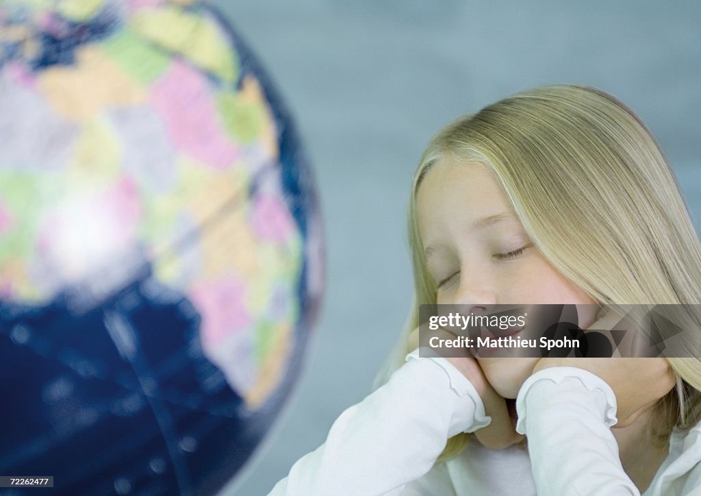 Girl next to globe, eyes closed