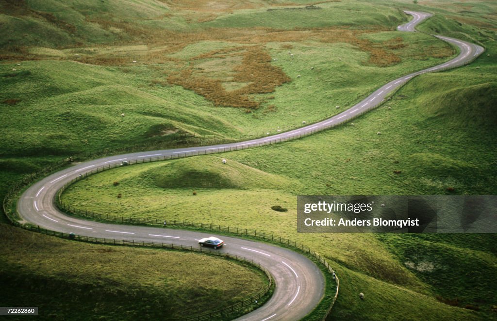 Car travelling down snaking road through grazing land of the Peak District, United Kingdom