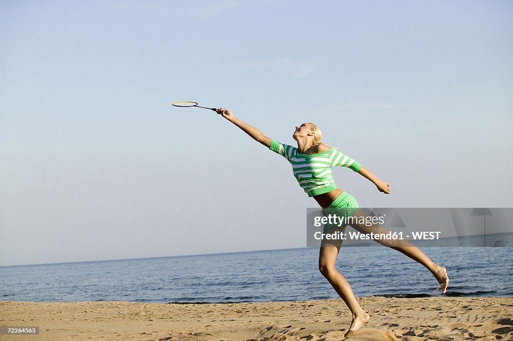 Young woman playing badminton on beach