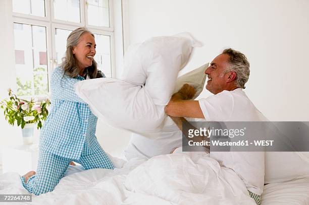 mature couple having pillow fight on bed - kissenschlacht stock-fotos und bilder