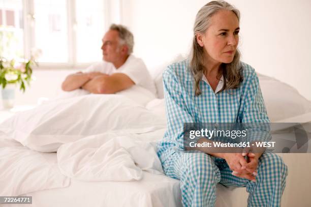 mature couple sitting on bed (focus on woman in foreground) - bored man in bed foto e immagini stock