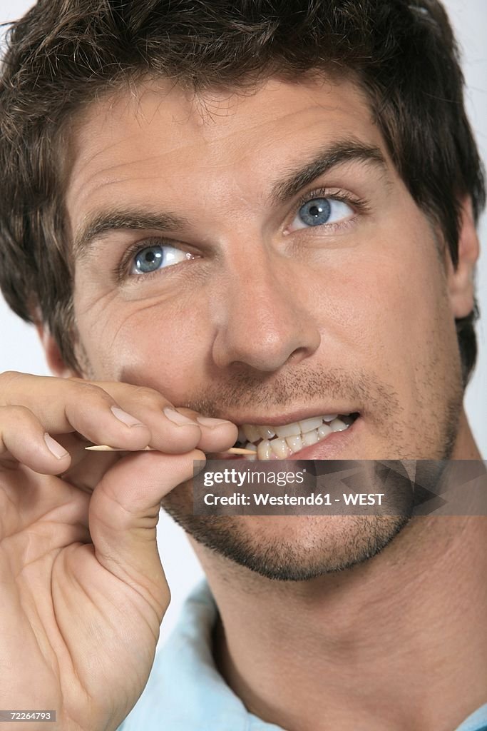 Young man holding toothpick between teeth, close-up