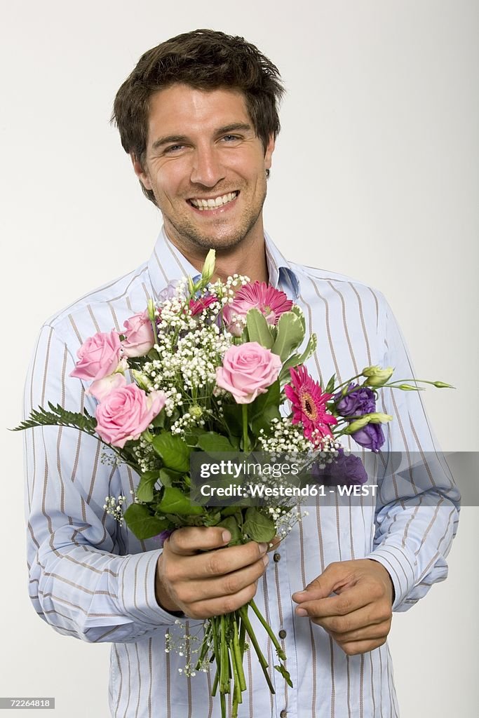 Young man holding bouquet of flowers, smiling, close-up, portrait