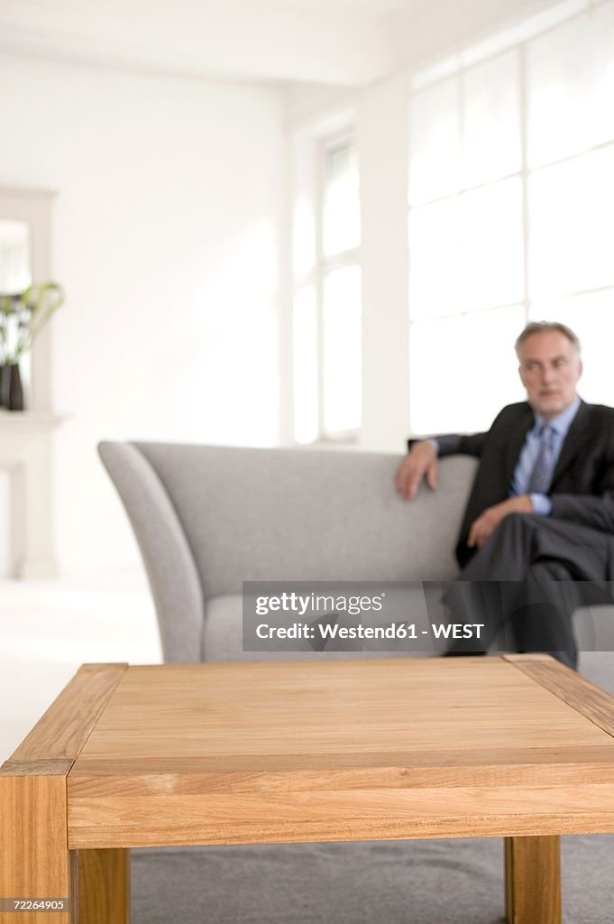 Mature man sitting on sofa, looking away (focus on table in foreground)