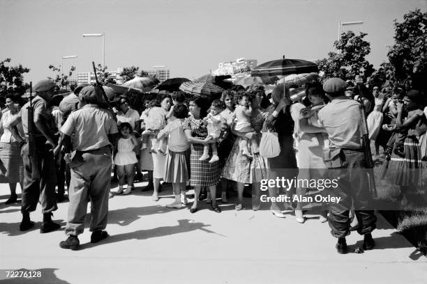 Month after the April, 1961 Bay Of Pigs invasion, armed militia men control a crowd of mothers, wives and children of POWs captured by Castro forces...