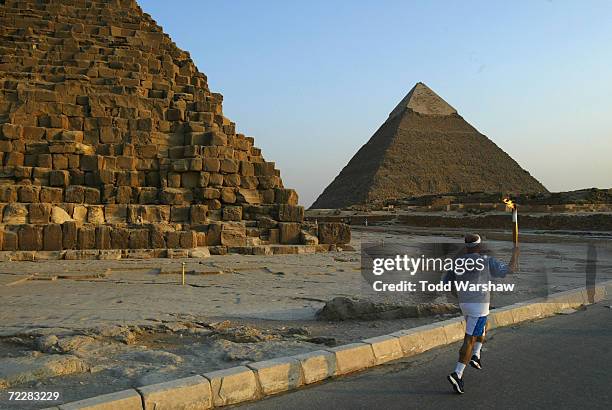 Torchbearer Nousier Mohamed carries the Olympic Flame past the Pyramids during Day 8 of the ATHENS 2004 Olympic Torch Relay on June 11, 2004 in...