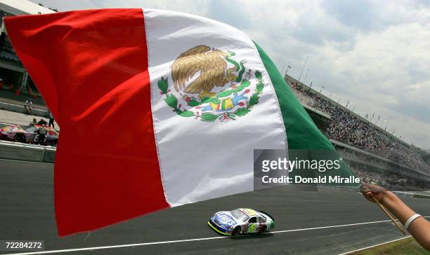 Adrian Fernandez of Mexico drives his Lowe's Chevrolet Monte Carlo as a fan waves the Mexican flag during qualifying for the Telcel Mexico 200 Nascar...