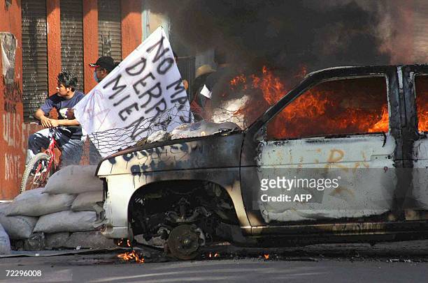 Members of the Oaxaca People's Popular Assembly hold banners behind a burnt car used to block a street in Oaxaca, Mexico, 29 October, 2006....
