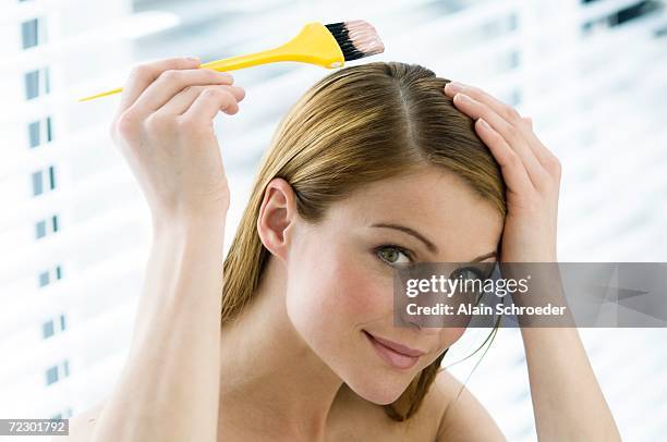portrait of a young woman dyeing her hair, little brush in her hand - tintura per capelli foto e immagini stock