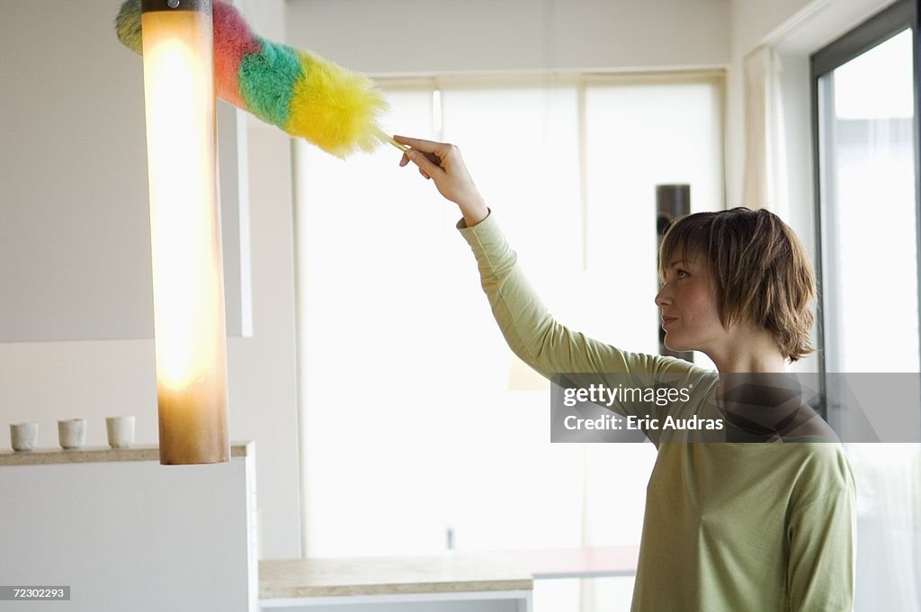 Woman dusting a lamp with a feather duster