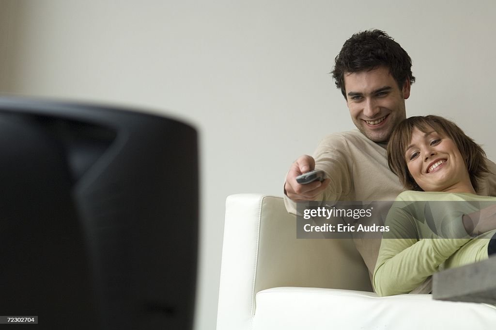 Smiling couple lying on a sofa, watching TV