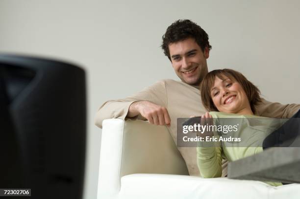 smiling couple lying on a sofa, watching tv - zappen stock-fotos und bilder