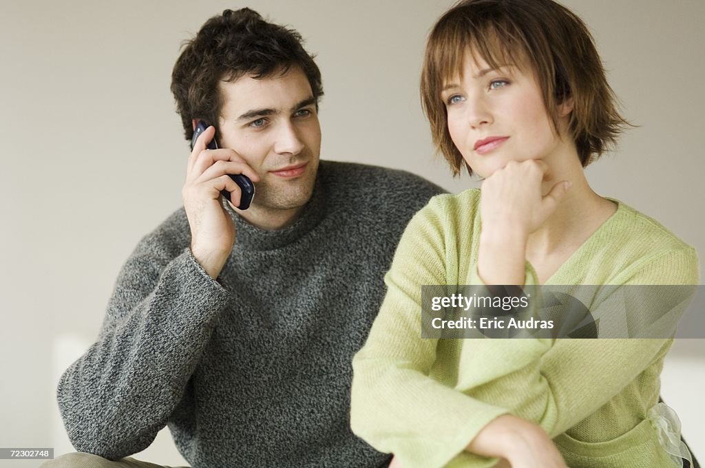 Couple sitting in living-room, man using a mobile phone