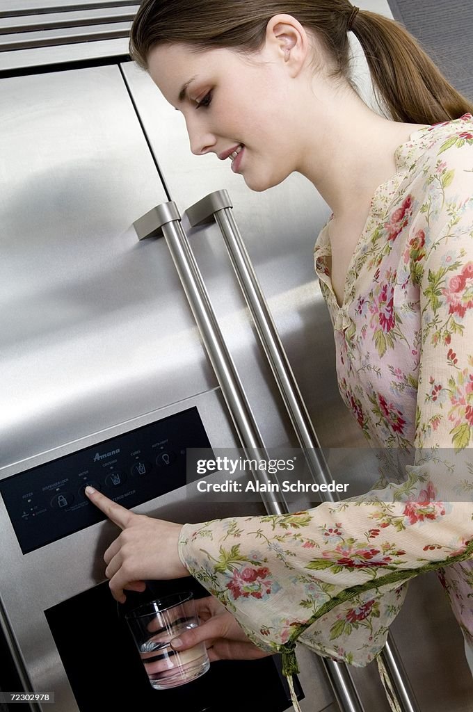 Young woman pouring water from a refrigerator water dispenser into a glass