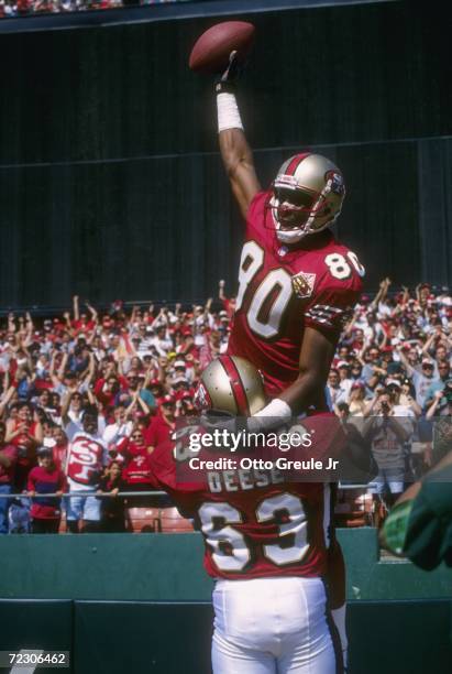 Wide receiver Jerry Rice of the San Francisco 49ers raises his arm in celebration as he is carried up by teammate Derrick Deese in the end zone...