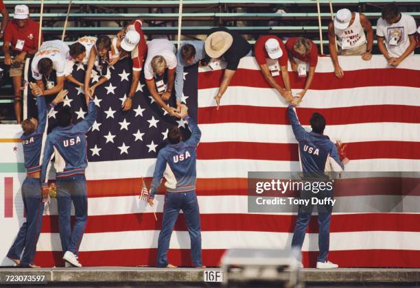 Chris Cavanaugh, Robin Leamy, David McCagg and Rowdy Gaines of the United States celebrate with fans in front of a large stars and stripes flag of...