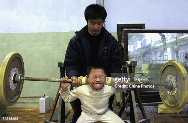 Young boy tries to lift a barbell with the help of his coach at Chengdu Children's Gymnastics School on January 11, 2005 in Chengdu, China. There are...