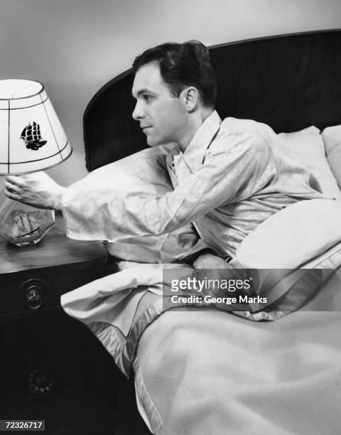 1950s: Man turning off bedside lamp.