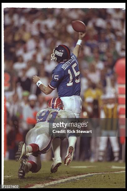 Quarterback Jeff Hostetler of the New York Giants throws the ball as he is being hit by linebacker Cornelius Bennett of the Buffalo Bills during...
