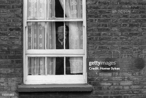 An old age pensioner looks out through the window of his flat in Whitechapel, 1975.