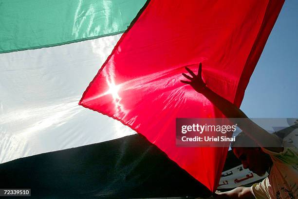 Palestinians carry their national flag next to the separation wall during a peace march August 27, 2004 in the West Bank town of Abu Dis on the edge...