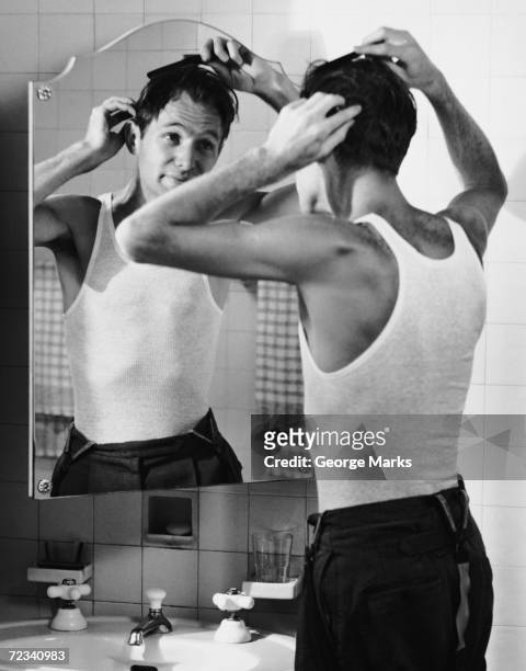 1950s: Man combing hair in bathroom.