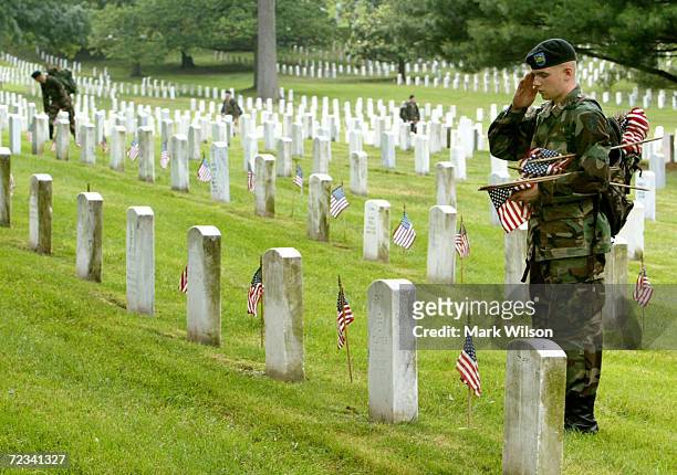 Member of the U.S. Army Infantry Regiment , salutes after placing a flag on a grave stone at Arlington National Cemetary May 27, 2004 in Arlington,...