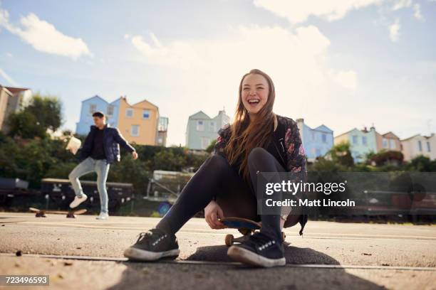 two friends fooling around outdoors, young woman sitting on skateboard, laughing, bristol, uk - bristol stock-fotos und bilder