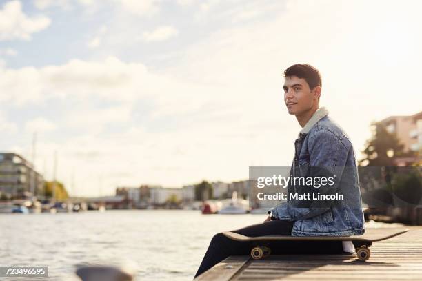 young man sitting by river, skateboard beside him, bristol, uk - bristol stock-fotos und bilder