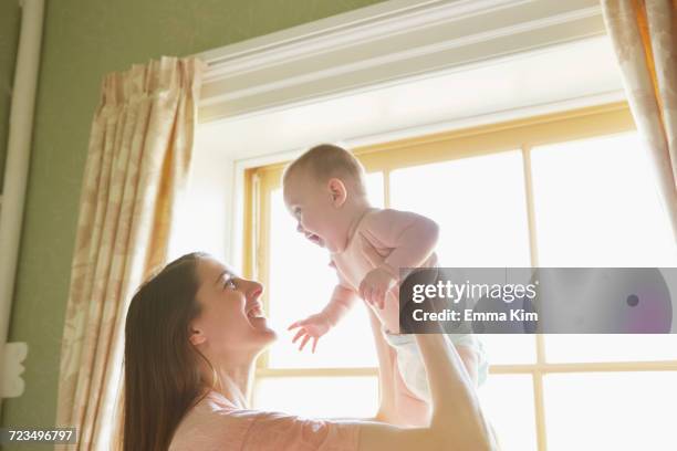 mid adult woman holding up baby daughter in bedroom - adult wearing diaper stock pictures, royalty-free photos & images