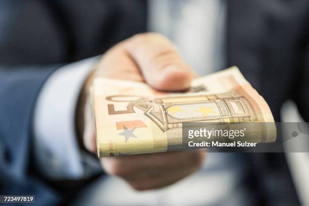 close up of businessmans hand handing folded fifty euro notes - bribing stockfoto's en -beelden
