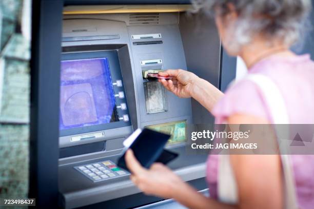 mature woman inserting credit card into local french cash machine - dab photos et images de collection