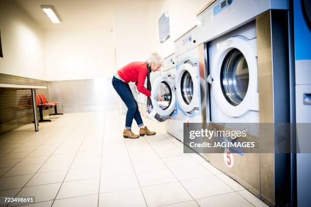 woman using washing machine in laundrette - older woman bending over stock pictures, royalty-free photos & images