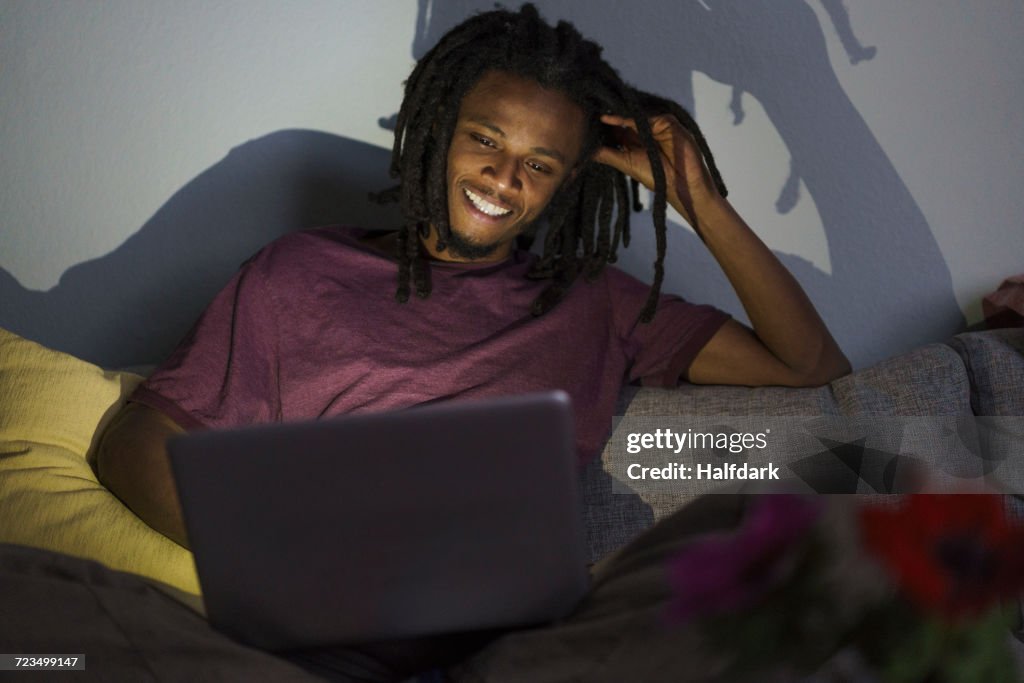 Happy man using laptop while sitting on sofa at home