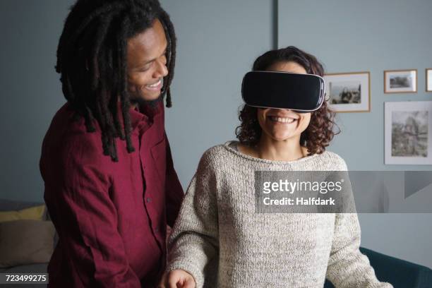 Happy man looking at woman using virtual reality headset in living room