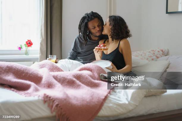 young woman kissing man while holding pie in bed at home - black couples kissing stock pictures, royalty-free photos & images