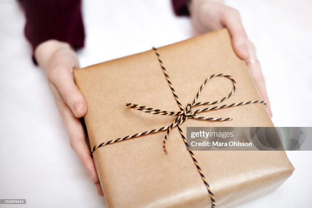 Woman holding gift wrapped in brown paper, decorated with string, close-up