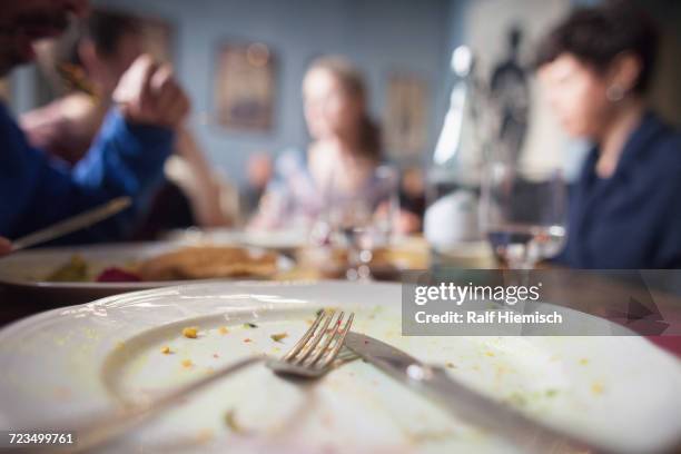 close-up of fork on plate with people sitting at dining table in background - leerer teller stock-fotos und bilder