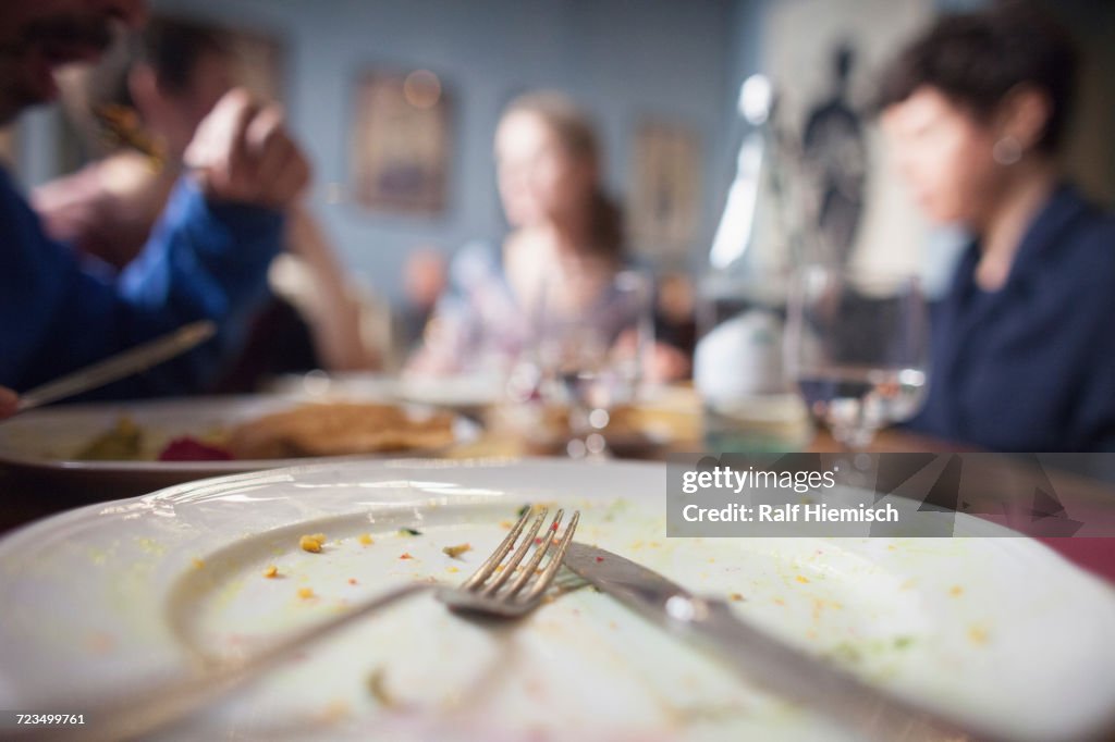 Close-up of fork on plate with people sitting at dining table in background