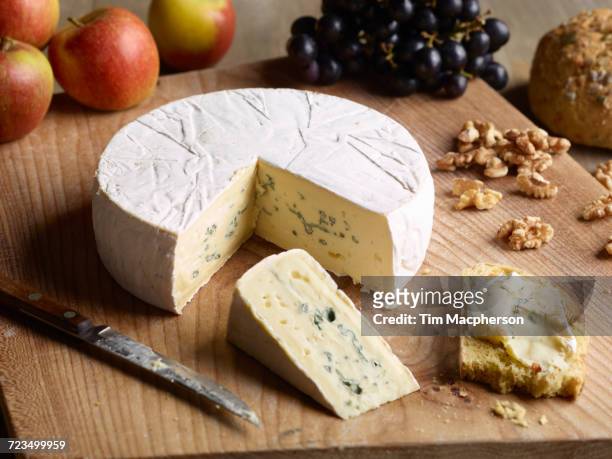 still life of blue brie with walnuts, grapes and apples on chopping board - wiel kaas stockfoto's en -beelden