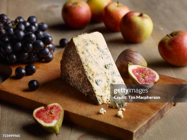 still life of stilton on chopping board with figs, apples and grapes - stilton stock-fotos und bilder