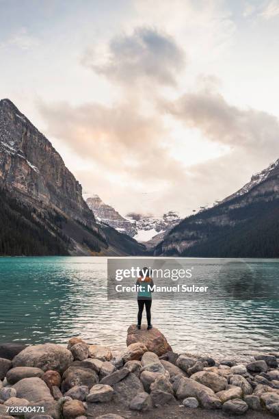 woman standing on rock, looking at lake view, rear view, lake louise, alberta, canada - see lake louise stock-fotos und bilder
