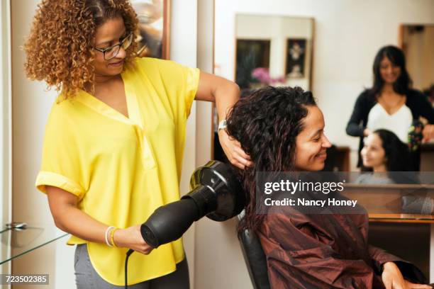 hairdresser blow drying female customers hair in hair salon - black hair stylist stock pictures, royalty-free photos & images