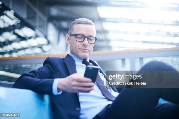 businessman on sofa looking at smartphone in office atrium - kompletter anzug stock-fotos und bilder