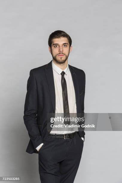 portrait of confident businessman standing with hands in pockets against gray background - maßanzug stock-fotos und bilder